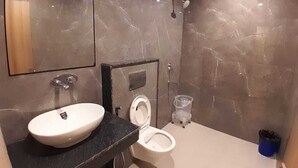 A modern bathroom with a marble wall, a sink, a toilet, and a shower. - Hotel Shiv Inn By T And M Hotels (Haridwar)