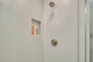 Ducha con panel de control en la pared y un estante pequeño con artículos de aseo.