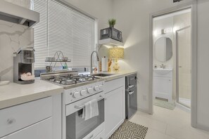 A modern kitchen with a gas stove, built-in oven, and a microwave. There is a sink, a countertop with a kettle, and a small plant on a shelf.
