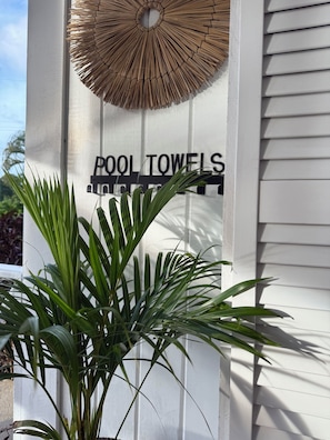 A sign for 'POOL TOWELS' with a decorative sunburst pattern above it, and a potted plant in the foreground. - Elegant Poolside Apartment, Large Covered Terrace- Walk to Beach, West Coast (Weston St James)