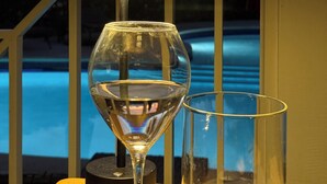 Un verre d’eau sur une table, avec une piscine et un coucher de soleil en arrière-plan.