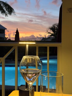 A glass of water on a table with a pool and sunset in the background.
