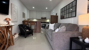 Un salon moderne avec un canapé gris, un fauteuil noir, une table basse en bois et un téléviseur fixé au mur.