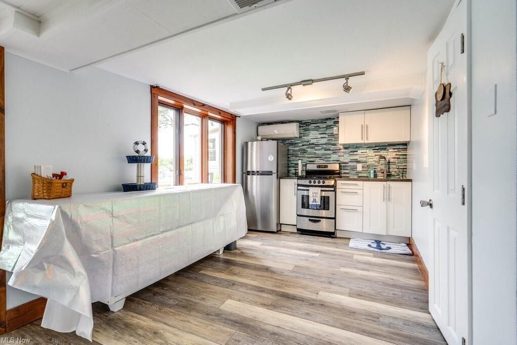 A compact kitchen with white cabinets, a stainless steel refrigerator, and a tiled backsplash.