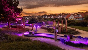 Un jardín arbolado con un sendero sinuoso, estructuras de madera y una hilera de casas al fondo.
