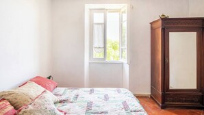 Ein Schlafzimmer mit Bett, Kleiderschrank und einem Fenster mit Blick auf Grünfläche.