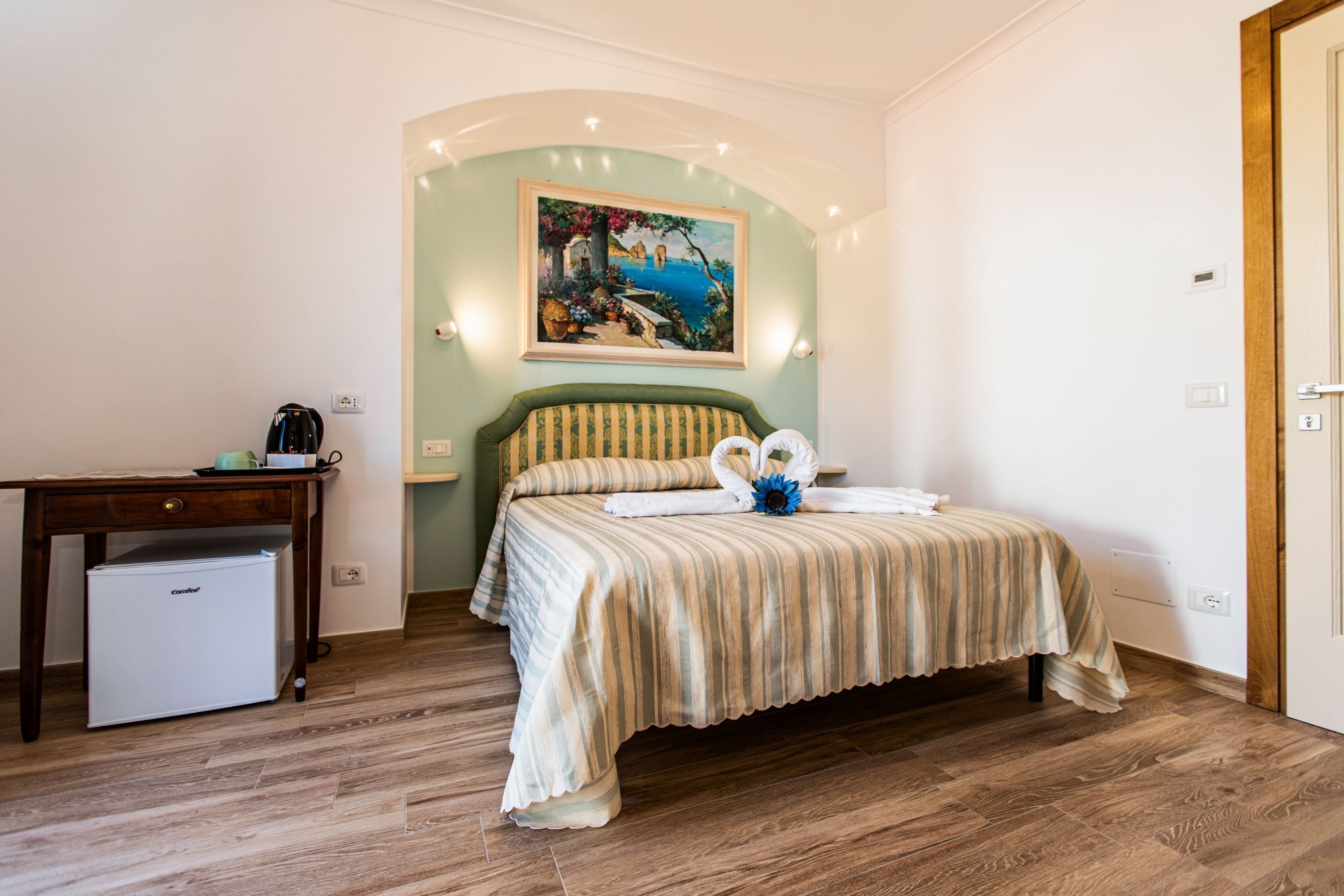 Un dormitorio con cama, escritorio, un refrigerador pequeño y un cuadro en la pared.