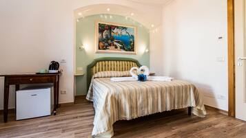 Un dormitorio con cama, escritorio, un refrigerador pequeño y un cuadro en la pared.