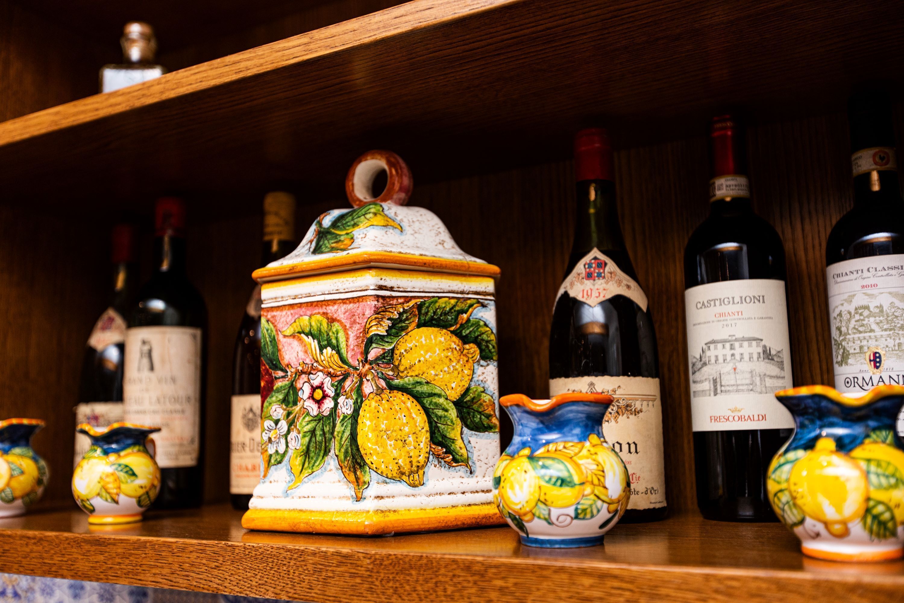 Une étagère en bois sur laquelle sont disposées différentes bouteilles de vin et des récipients en céramique.