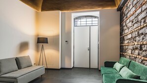 Ett rum med en soffa i rutmönster, en grön soffa, en golvlampa och en vägg av tegelsten.