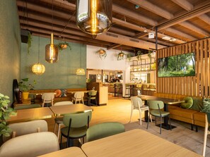 A modern restaurant with wooden beams, green upholstered seating, hanging pendant lights, and a large TV on the wall. - Bungalow in De Peel by Tranquil Forest (Vlierden)