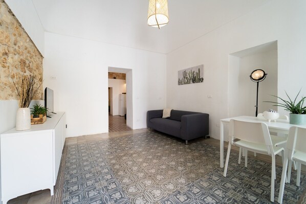 A modern living room with a grey sofa, white dining table, and patterned floor tiles. - Dimora Netina by Wonderful Italy (Noto)