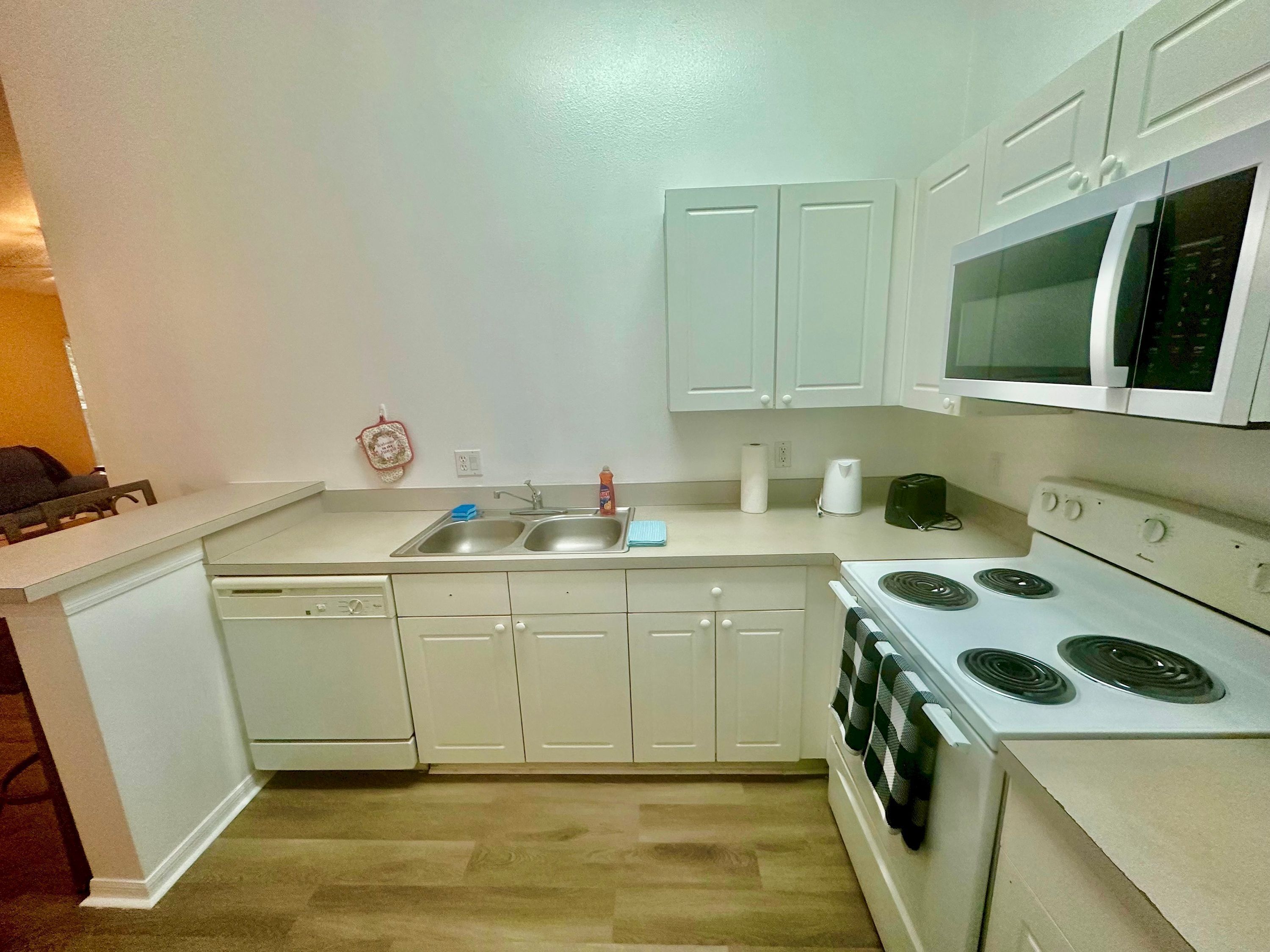 A compact kitchen with white cabinets, a dishwasher, a stove, and a microwave.