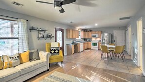 A spacious living area with a sofa, yellow armchair, dining table, and kitchen in the background.