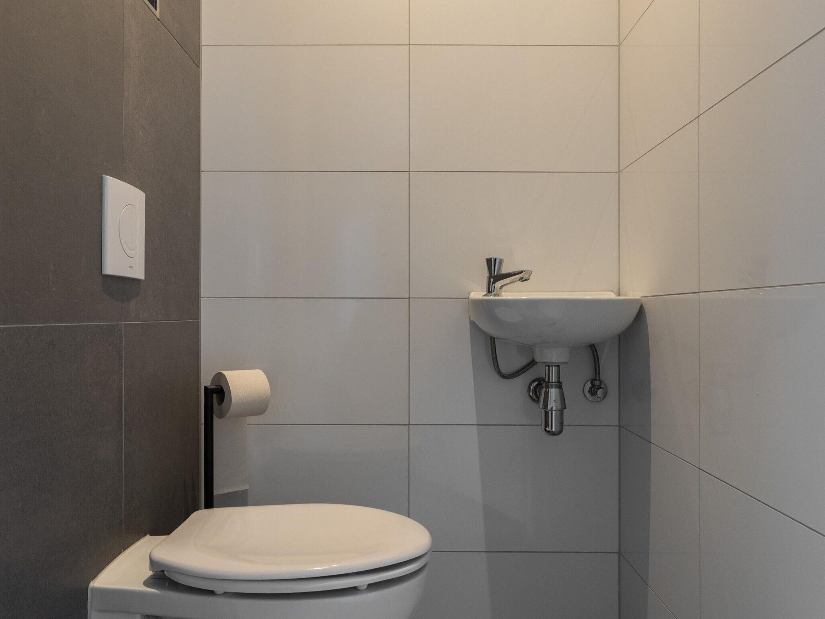 Un baño moderno con inodoro, lavamanos y dispensador de papel higiénico.