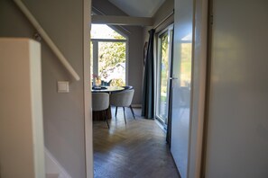 A hallway leading to a dining area with a table and chairs, a window with curtains, and a door. - Eco Villa in Latour by Scenic Pond (Oirschot)