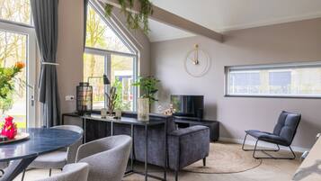 A modern living room with a dining area, large windows, and a TV.
