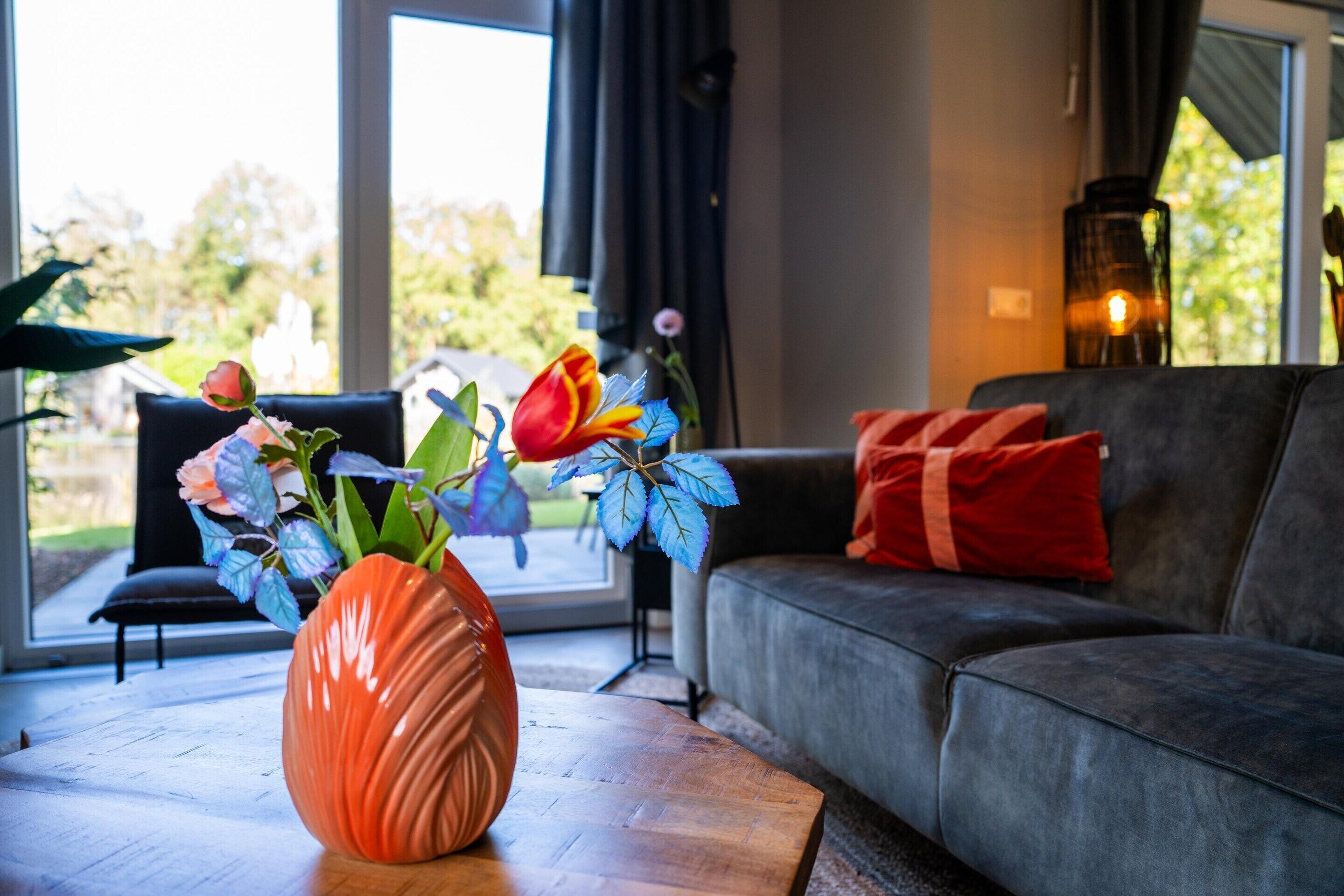 Een woonkamer met een grijze bank, een houten salontafel en een vaas met bloemen.