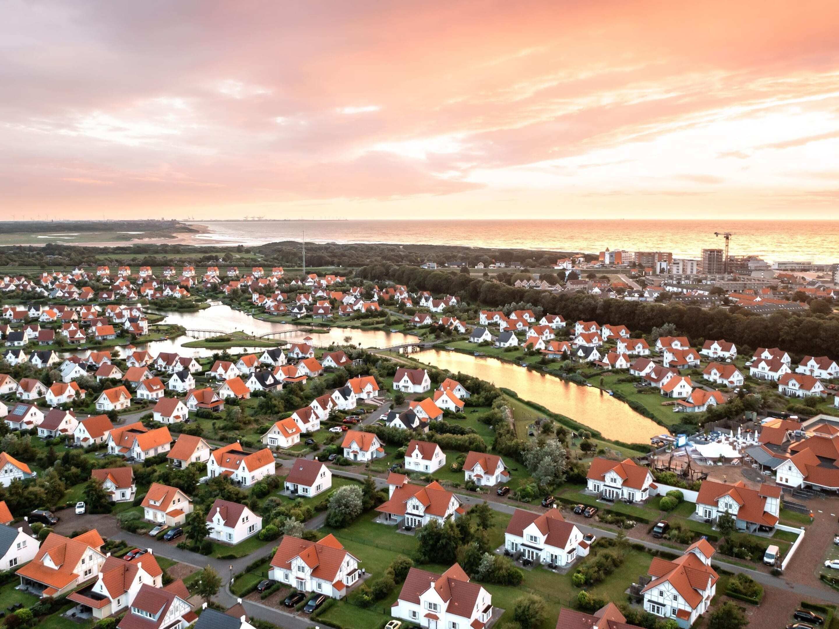 Vista aérea de una zona residencial con casas, un río y una zona industrial distante al atardecer.