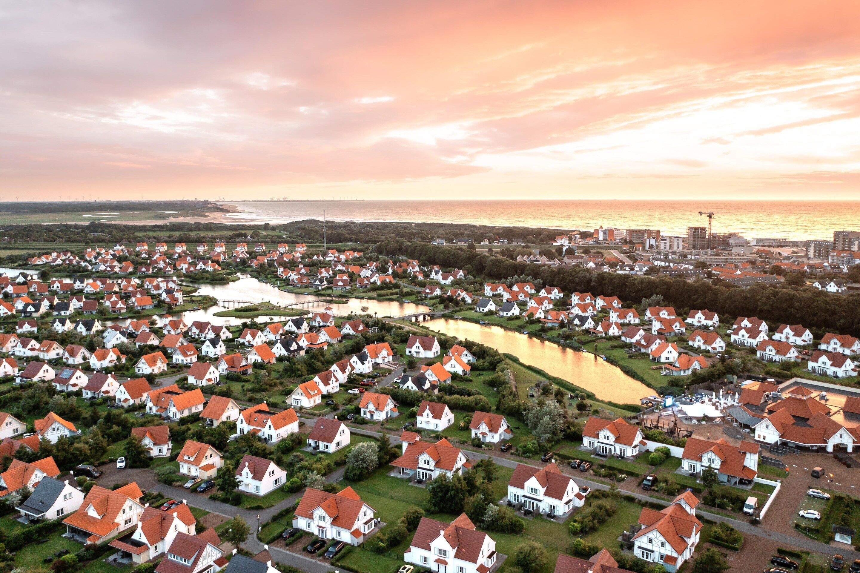 Luchtbeeld van een woonwijk met huizen, een meer en een verafgelegen stadsgezicht.