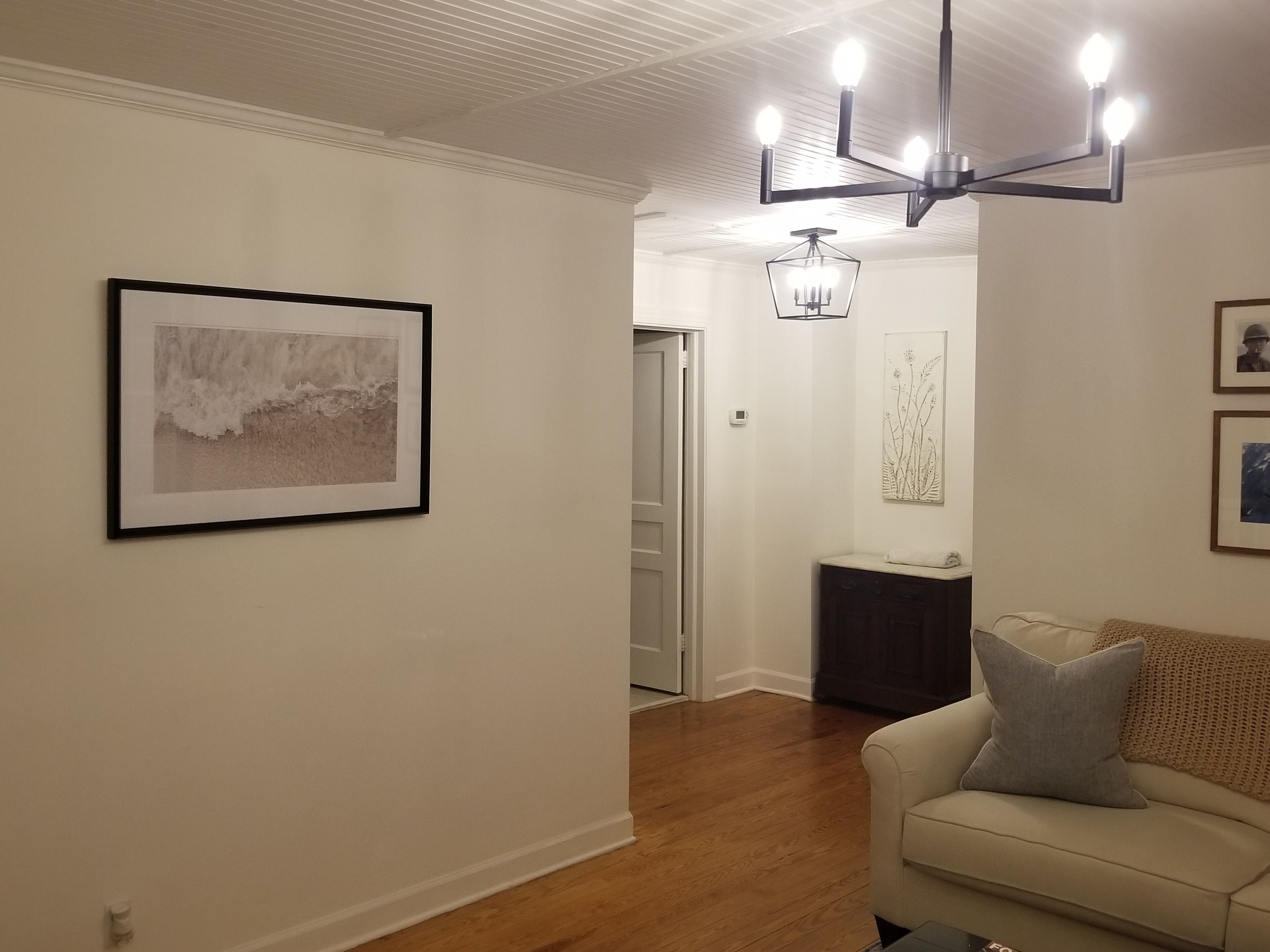 Una sala de estar con un sofá color beige, una araña y cuadros en las paredes.
