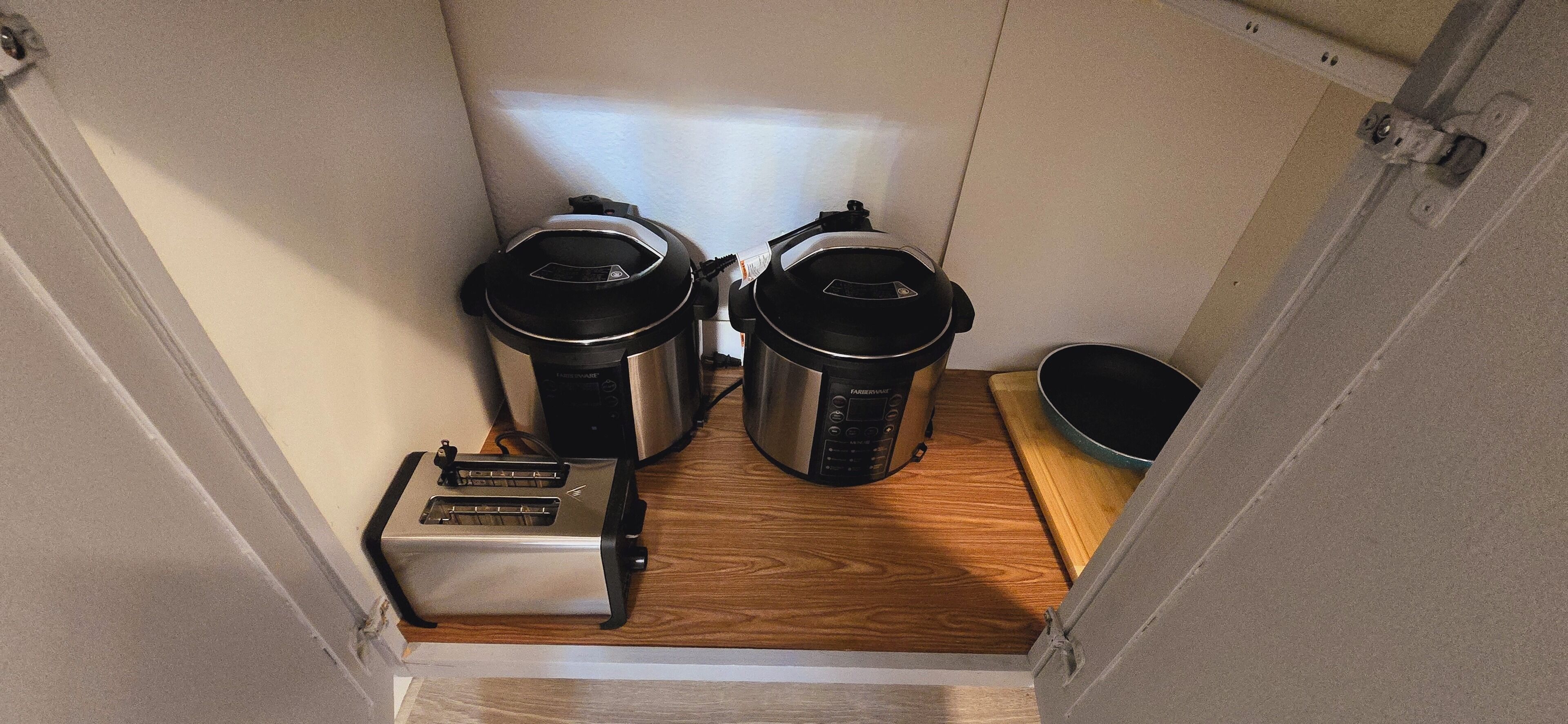 Una piccola cucina compatta con due pentole a pressione elettriche, un tostapane e un lavandino.
