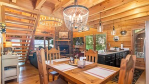 A wooden cabin interior with a dining table, chairs, a chandelier, a fireplace, and a kitchen area. - Haven Overlook a true Mountain Luxury (Blueridge)