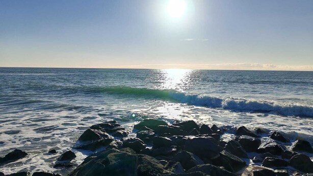 A beach with waves crashing onto rocks under a clear sky.