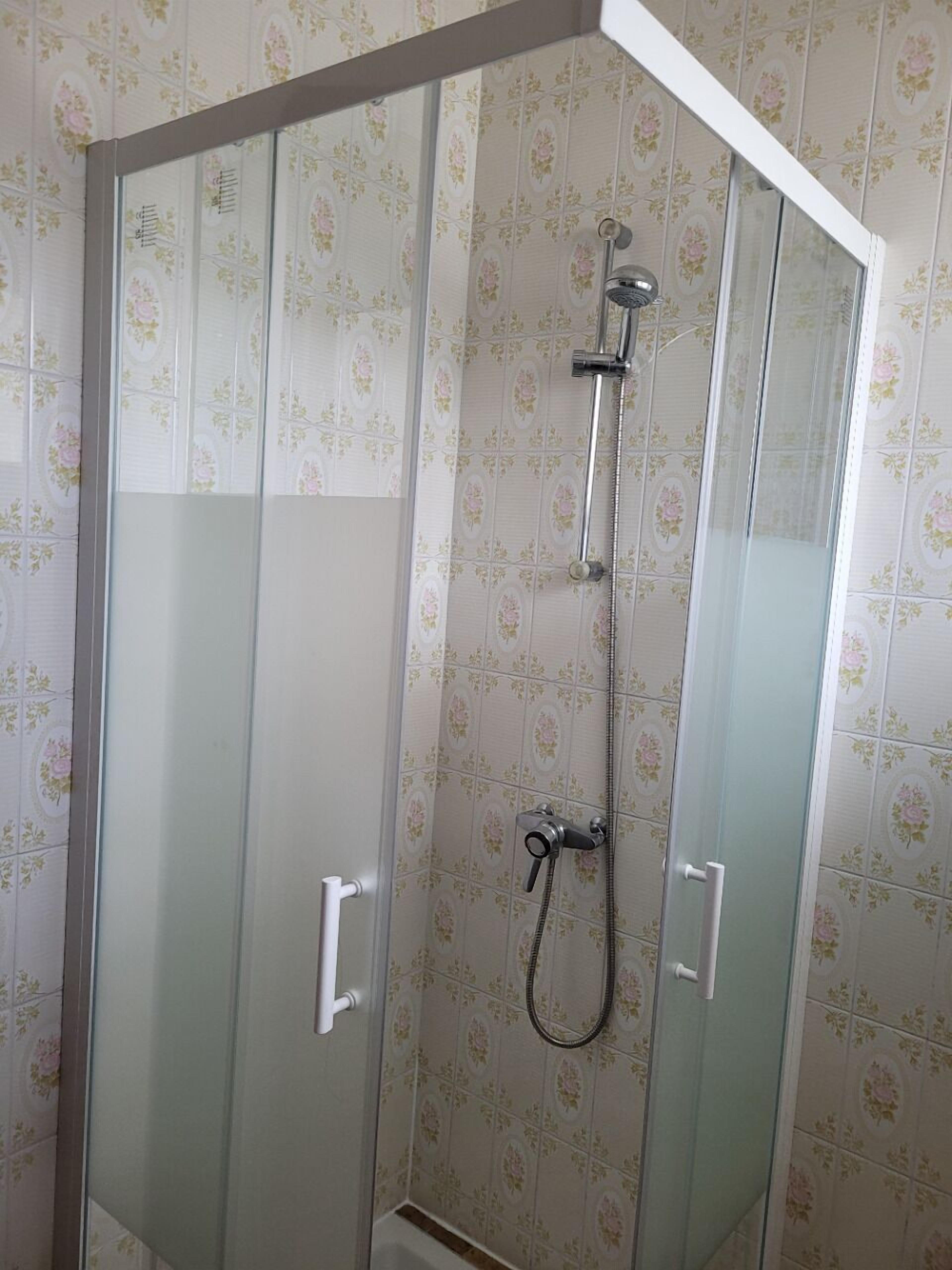A glass-enclosed shower stall with a handheld showerhead and a wall-mounted faucet.