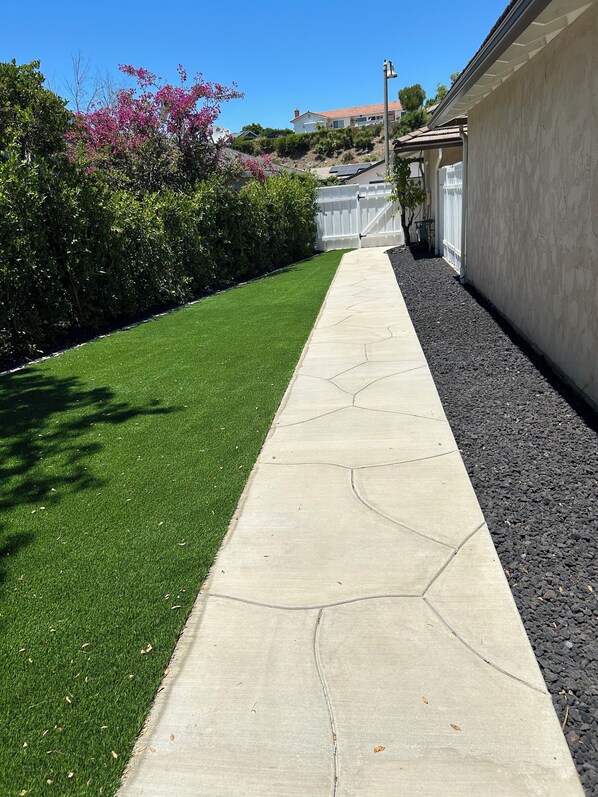 A well-maintained pathway with a green lawn on one side and a gravel area on the other, leading to a building with a white fence and a clear blue sky in the background. - "The Best" Jacuzzi View Private Luxury Guest Cottage-Better than a Room or Suite (Thousand Oaks)