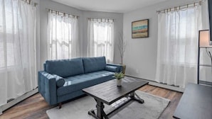 Ein Wohnzimmer mit einem blauen Sofa, einem Holztisch und weißen Vorhängen.