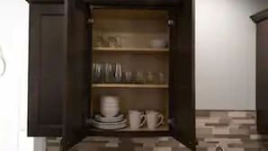 Eine Küche mit einem dunklen Holzschrank, offenen Regalen mit Geschirr und Gläsern sowie einer gefliesten Spritzschutzwand.