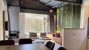 A modern living room with a fireplace, comfortable seating, and a large window with a view of trees. - Bungalow on Weerterbergen Waterfront (Weert)