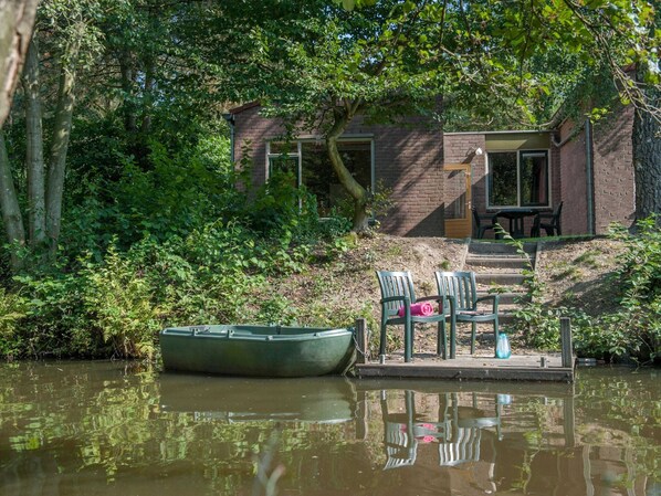 A riverside cabin with a dock, chairs, and a table.
