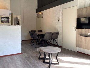 A modern kitchen with a dining area, featuring a round table with chairs, a hanging light fixture, and a built-in TV.