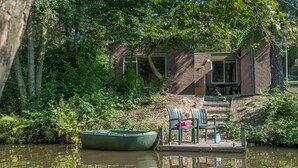 A riverside setting with a dock, a boat, and a building with a patio. - Bungalow on Weerterbergen Waterfront (Weert)
