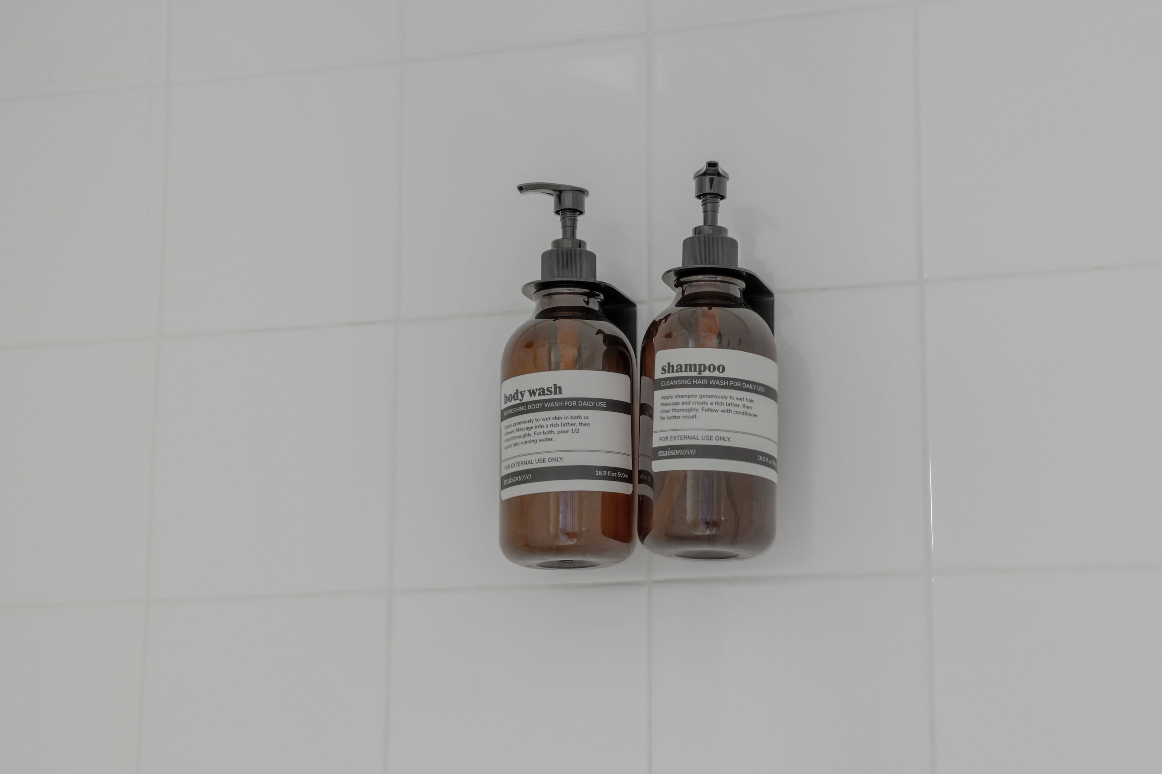 Two brown bottles with pumps on a white tiled wall.