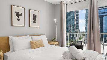Una habitación de hotel moderna con una cama grande, una mesita de noche, una lámpara y dos cuadros enmarcados en la pared.