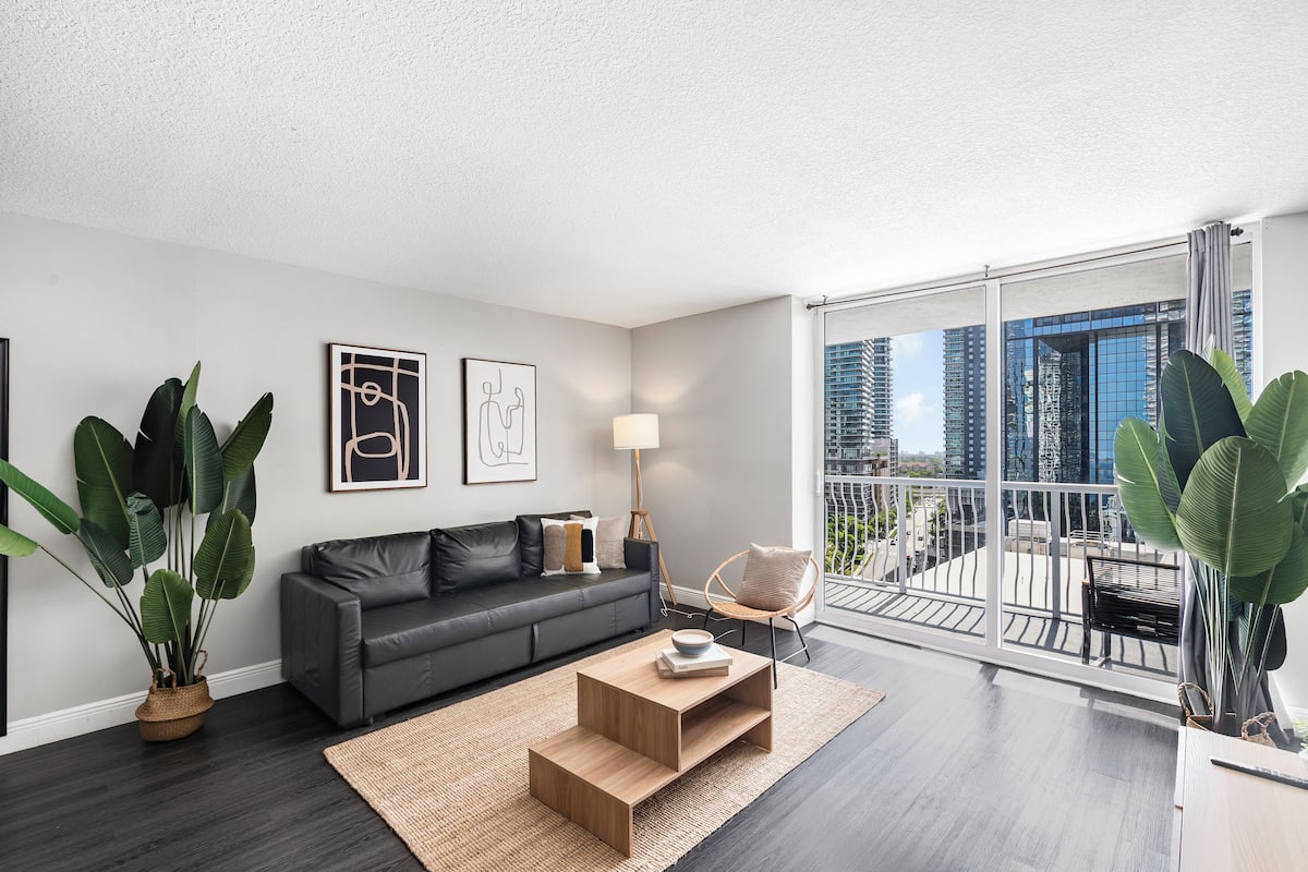 A modern living room with a grey sofa, a wooden coffee table, and large potted plants.