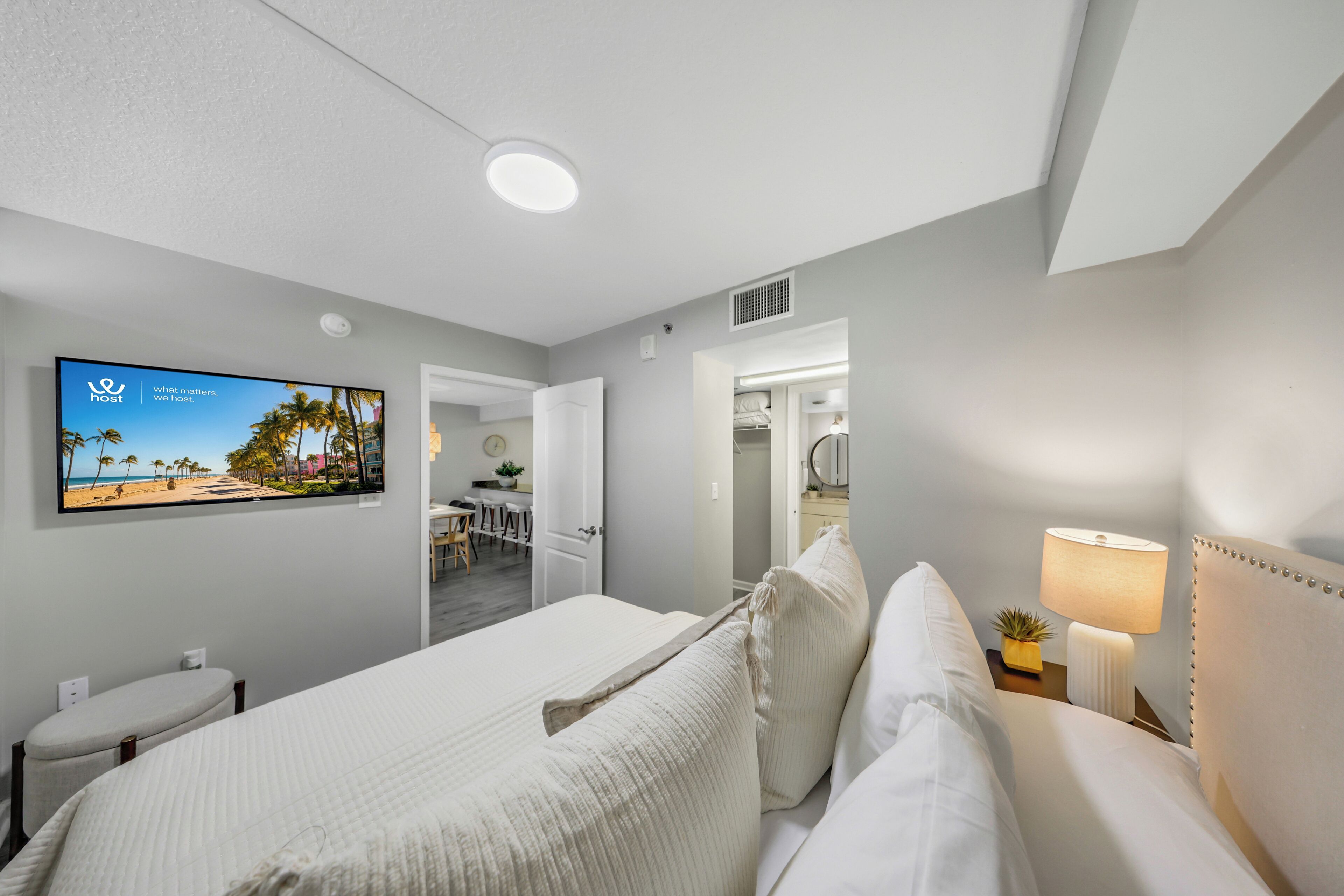 Een hotelkamer met een bed, een televisie aan de muur, een nachtkastje met een lamp, en uitzicht op het strand door het raam.