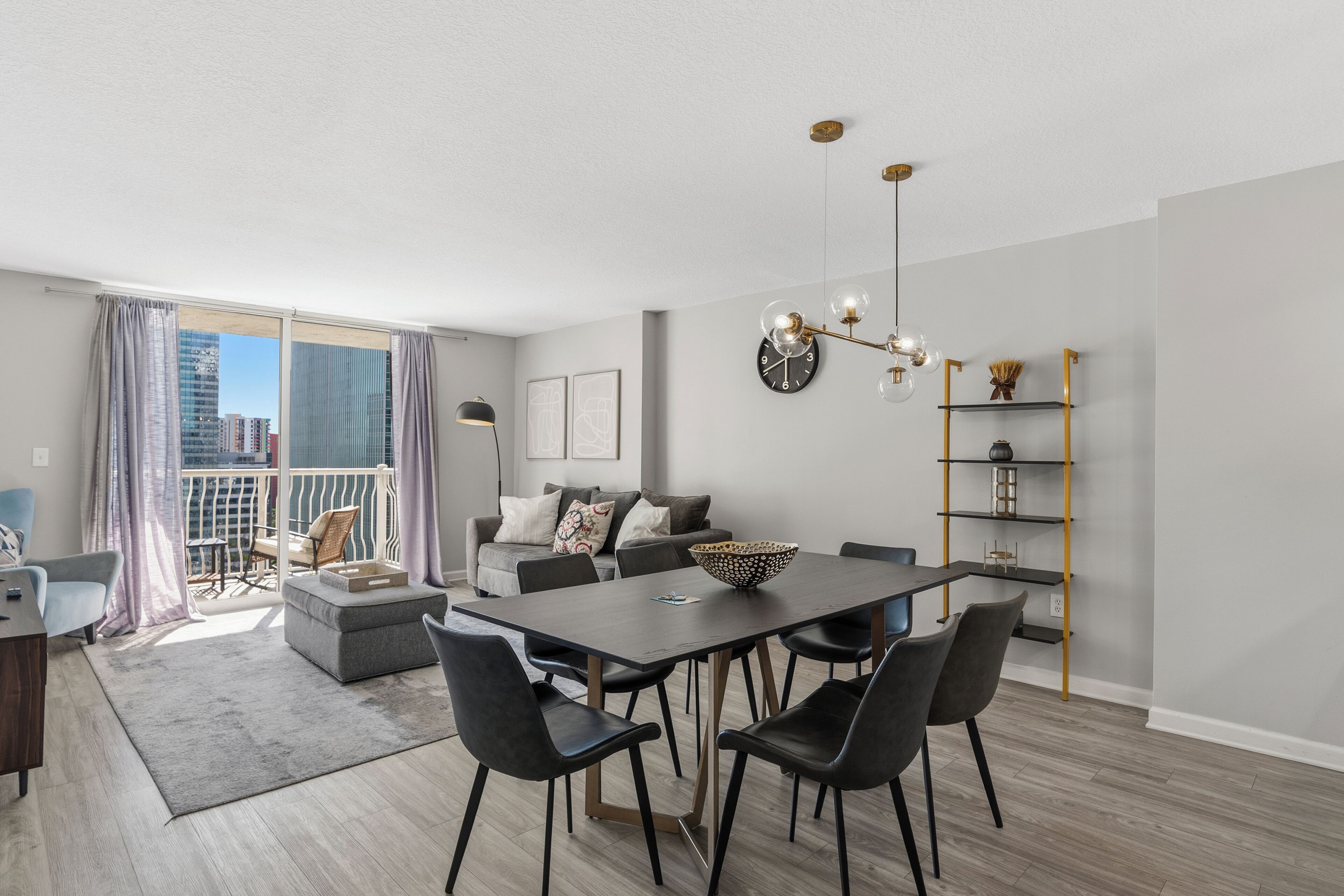 Una sala moderna con una mesa de comedor, sillas, un sofá y un balcón con cortinas.