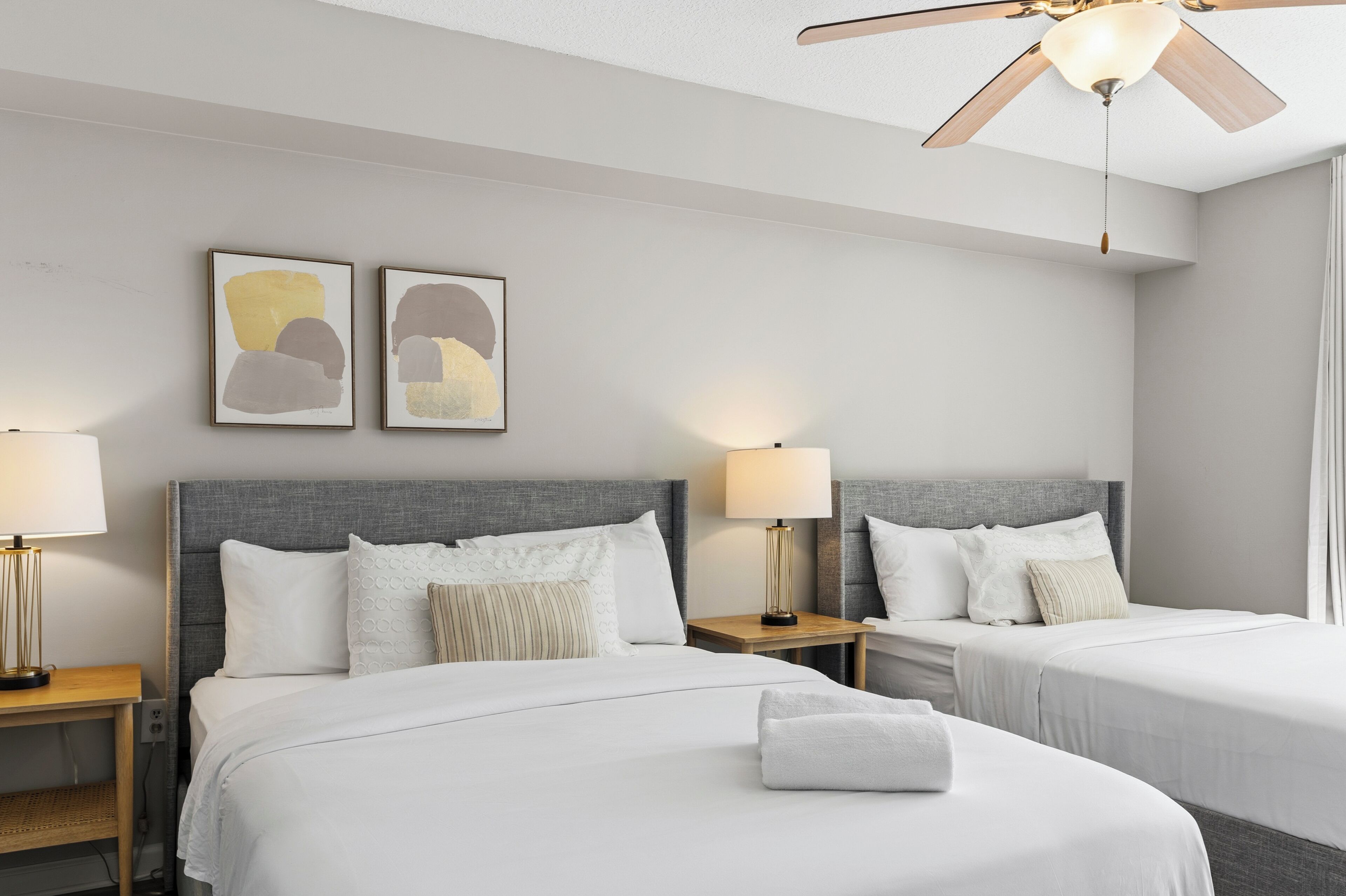 Ett hotellrum med två sängar, en takfläkt, konst på väggarna och sänglampor.