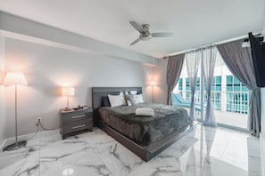 A modern hotel bedroom with a large bed, two bedside lamps, a ceiling fan, and a view of a building through sheer curtains.