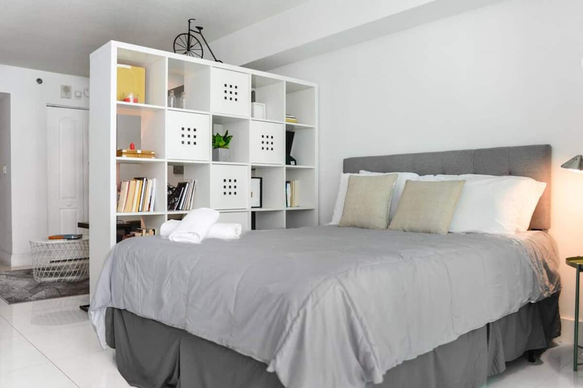 A bedroom with a large bed, a white storage unit, and a bicycle on the ceiling.