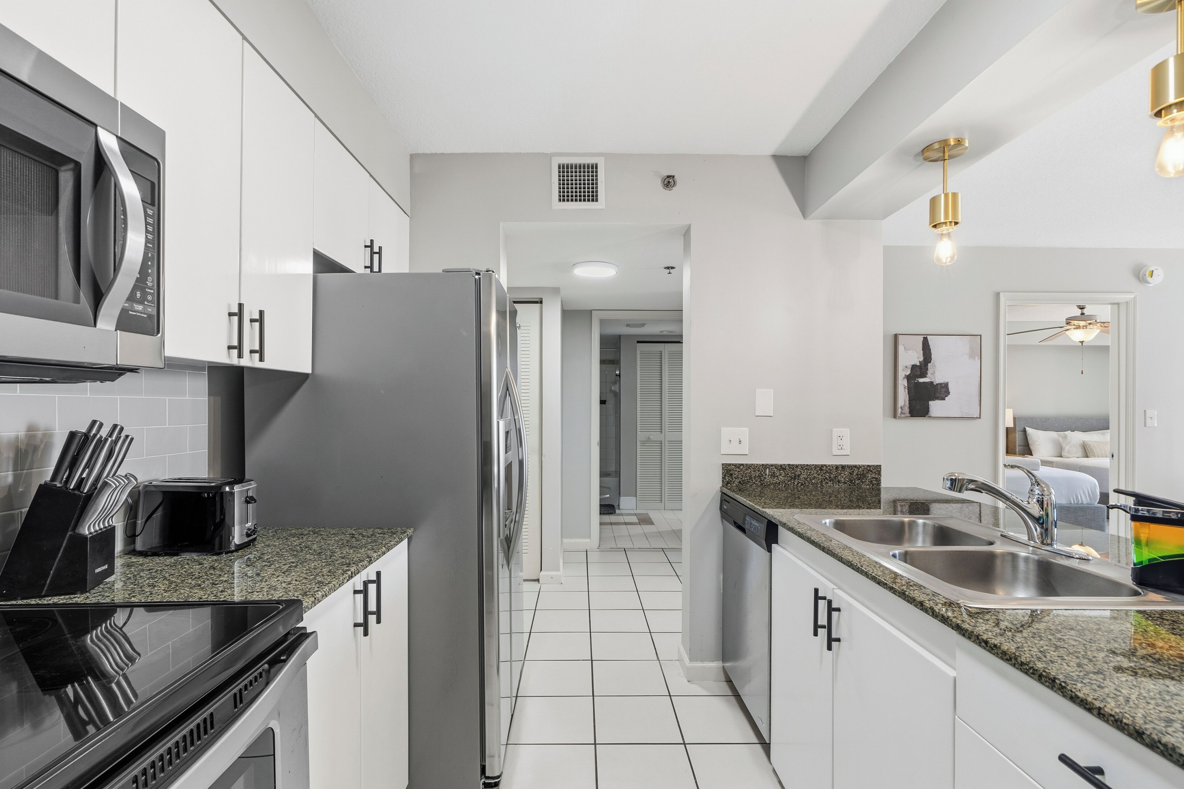 A modern kitchen with white cabinets, stainless steel appliances, a granite countertop, and a built-in dishwasher.