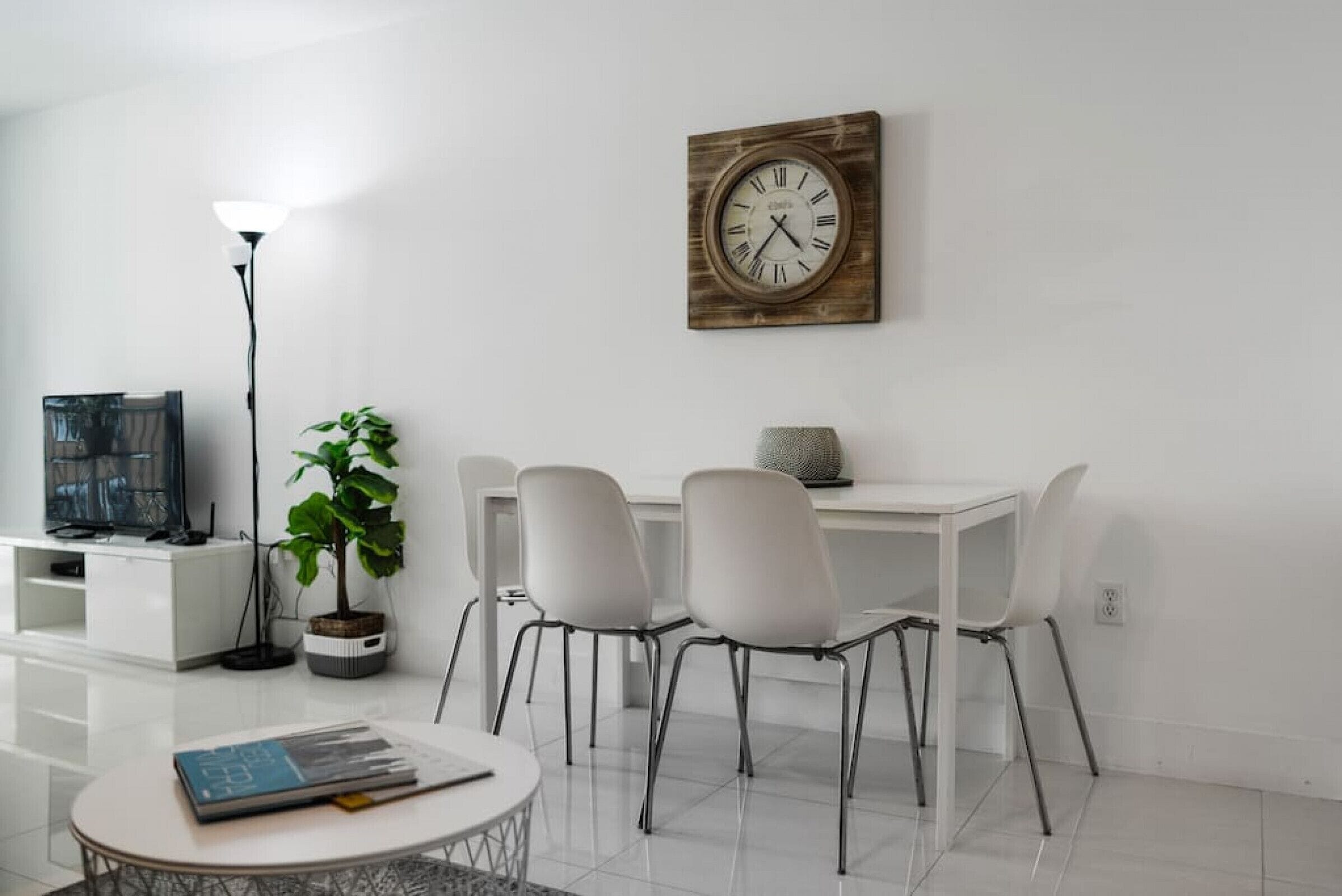 Una sala moderna con comedor, televisor, planta en maceta y un reloj en la pared.