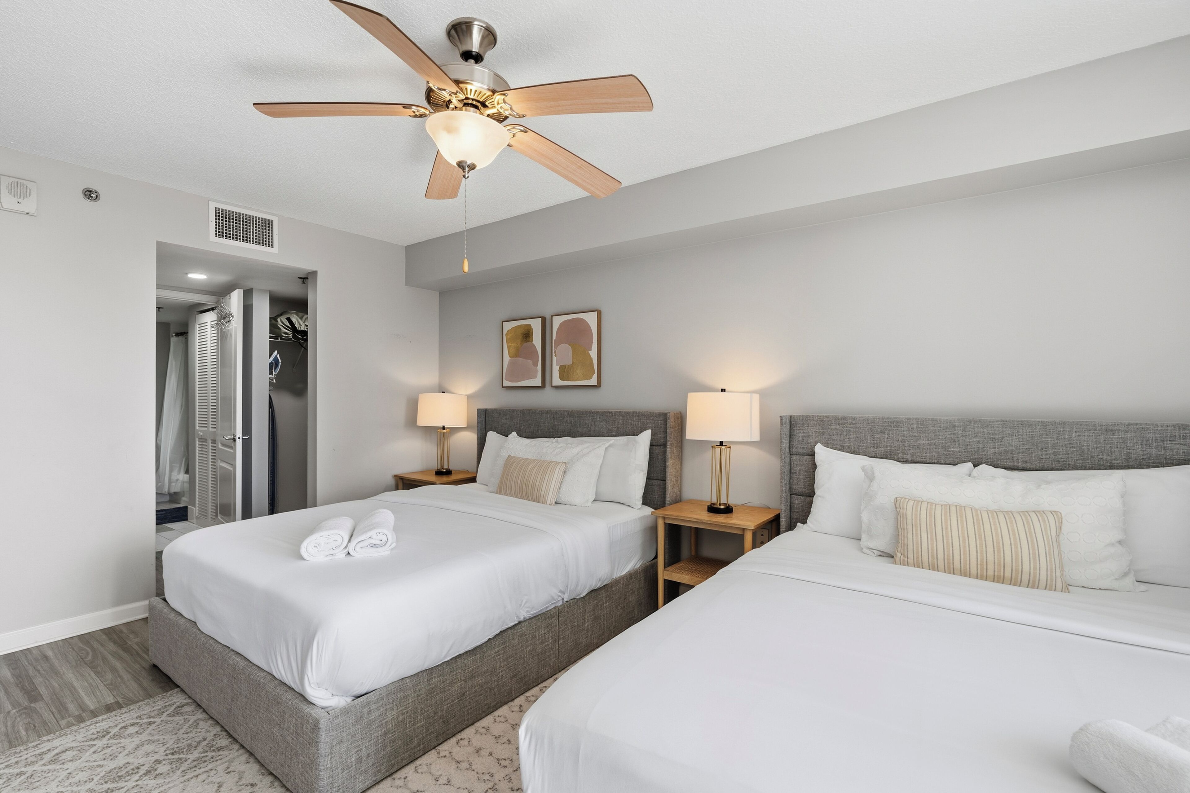 Quarto de hotel com duas camas, um ventilador de teto e área de chuveiro.