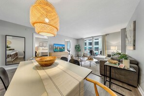 En moderne stue med spiseplads, sofa, sofabord og et stort vindue.