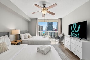 A modern hotel room with two beds, a ceiling fan, a TV, and a city view.