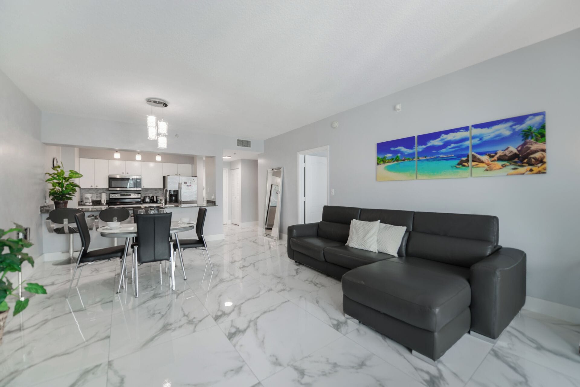 A modern living room with a black leather sofa, a dining area with a glass table and chairs, and a kitchen in the background.